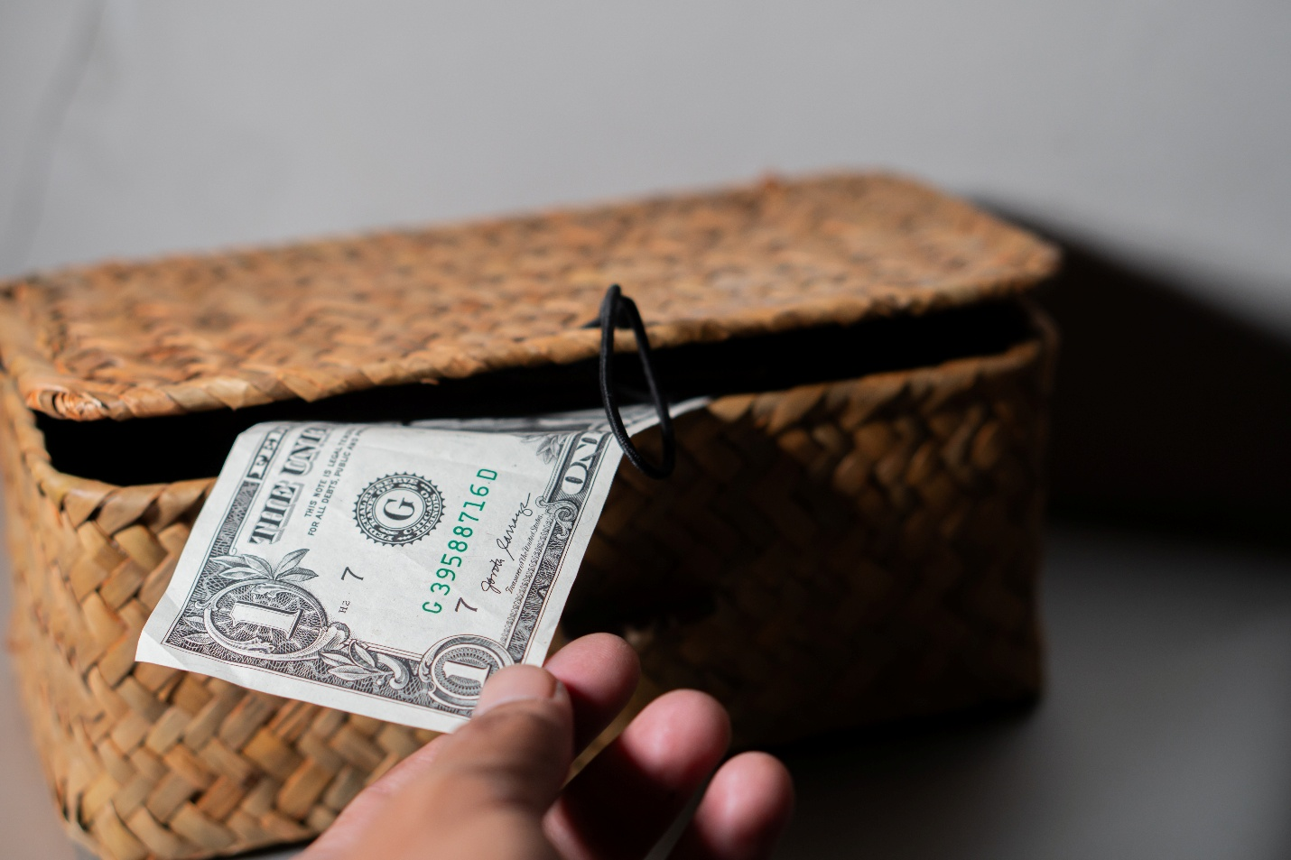 A hand placing a one-dollar bill into a woven wicker donation box.