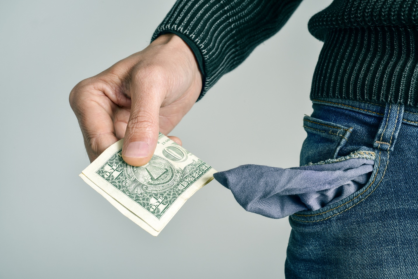 A person pulling a single one-dollar bill out of their denim jeans pocket.